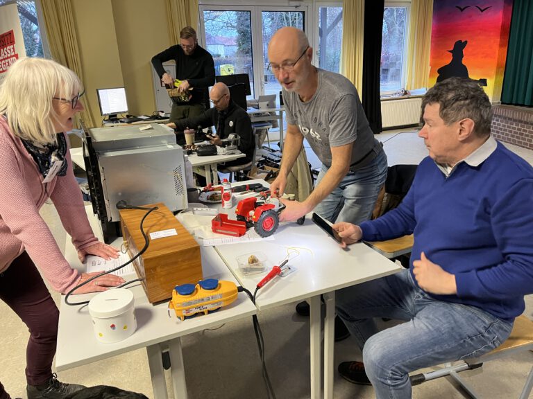 Zwei Herren und eine Dame reparieren einen Spielzeugtraktor ZT 300