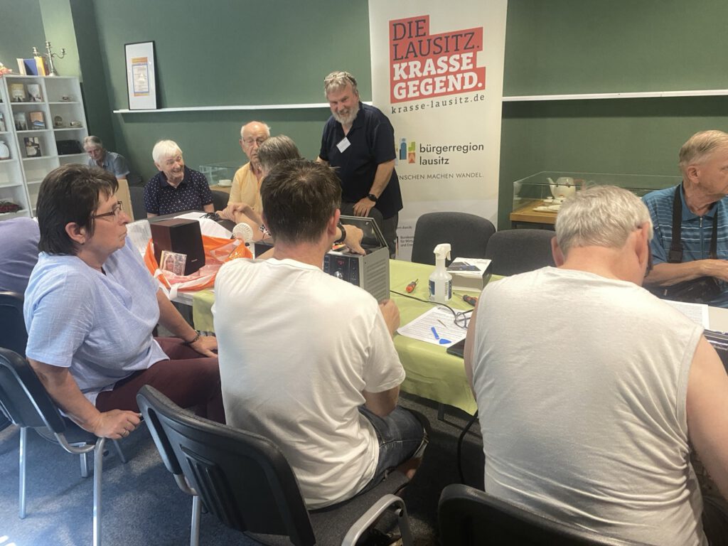 Eine Gruppen Menschen sitzt um einen Tisch und repariert Geräte